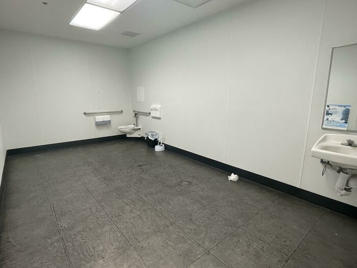 A bare, stark public restroom with a single toilet and sink, an unsettling liminal space.