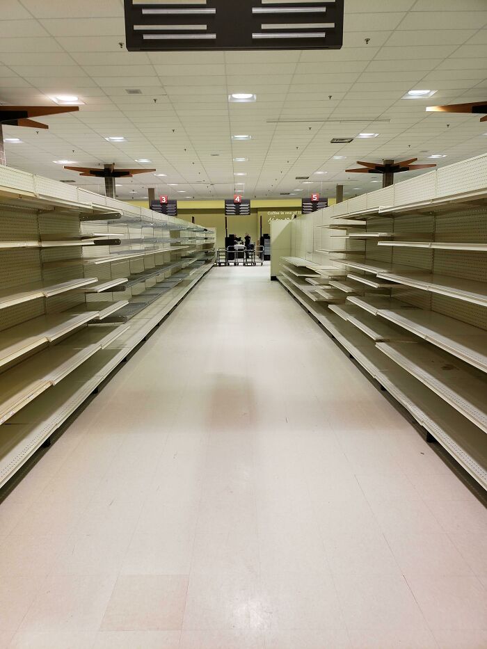 Empty supermarket aisles with bare shelves extend into the distance, a deeply unsettling liminal space.