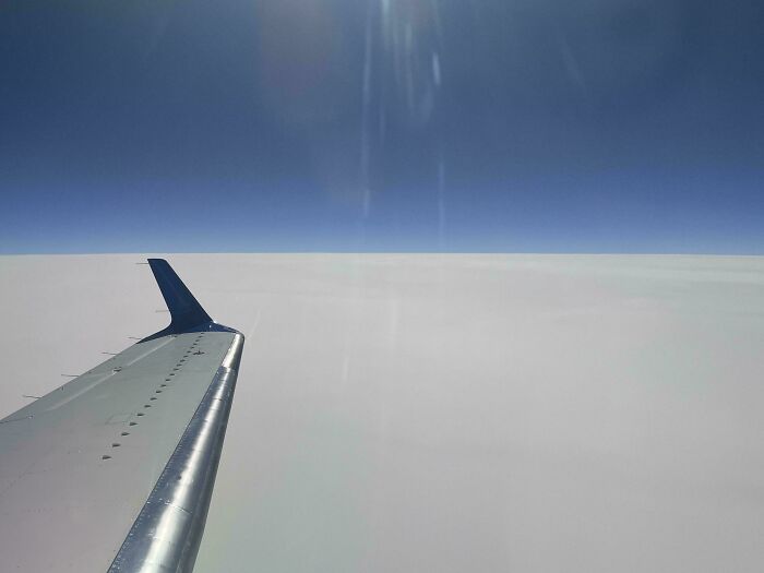 Airplane wing soaring above thick clouds, a deeply unsettling liminal space.
