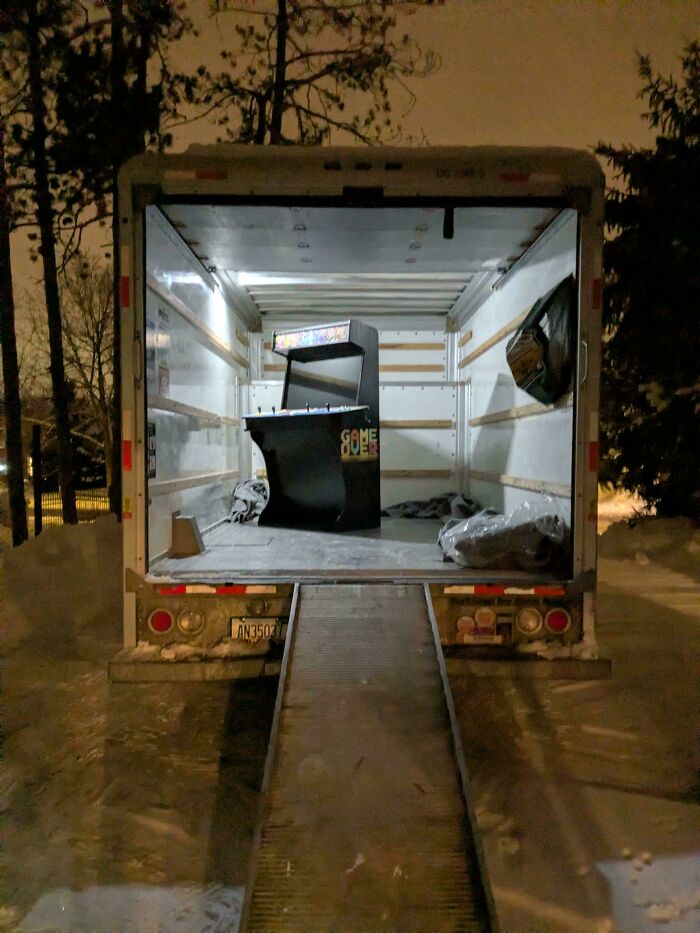 A lone arcade machine sits in the back of an empty moving truck, creating a deeply unsettling liminal space.