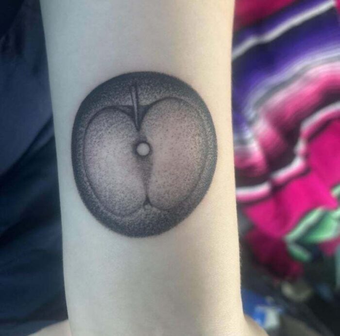 Black ink tattoo fail resembling a peach on person's arm