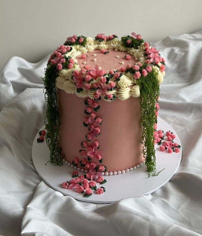Pink floral cake decorated with cascading cream flowers and green leaves