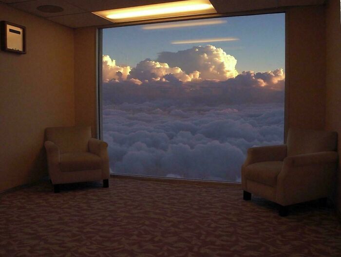 Two armchairs in a room with a window overlooking a vast expanse of clouds, an unsettling liminal space.