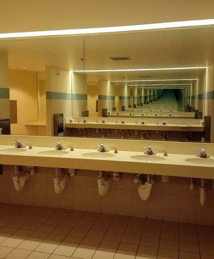 A long row of bathroom sinks with mirrors reflecting into infinity, creating a surreal and unsettling liminal space.