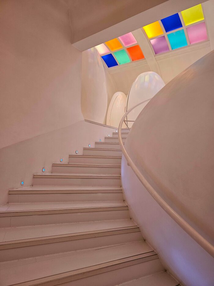 A winding white staircase with colorful stained-glass windows above, creating a unique liminal space.