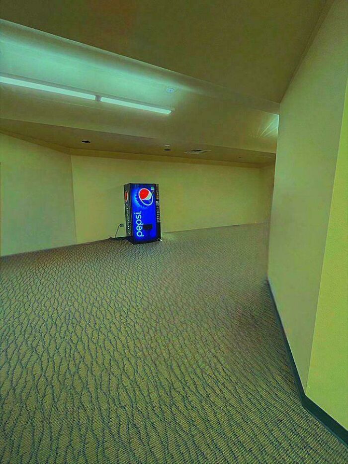 A solitary Pepsi vending machine in an empty, carpeted hallway, a deeply unsettling liminal space.
