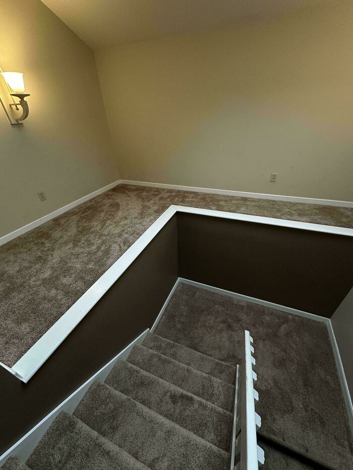 A view of stairs leading down to a lower level, featuring light brown carpet and plain walls, depicting a liminal space.