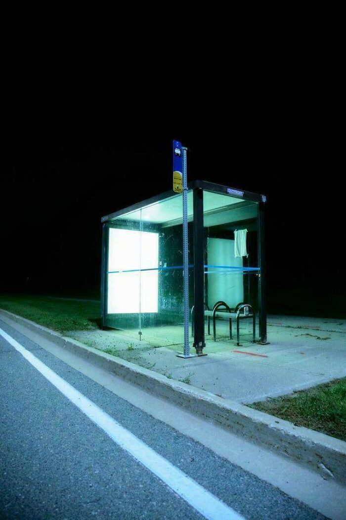 A stark, illuminated bus stop at night, creating a deeply unsettling liminal space.