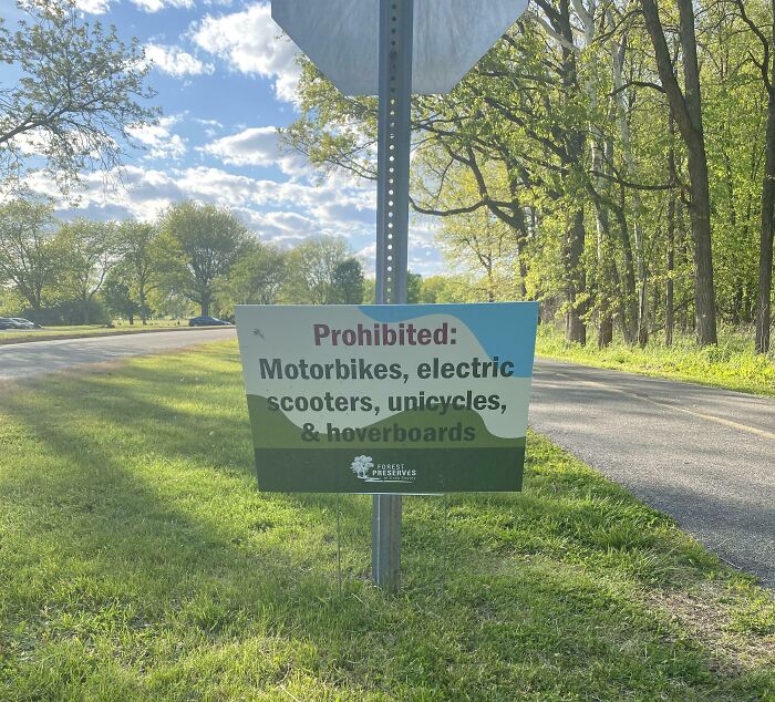 A funny sign in the wild prohibiting motorbikes, electric scooters, unicycles, and hoverboards in a forest preserve.