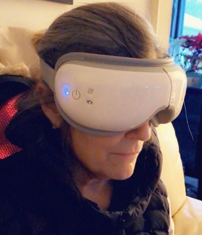 A person wearing a white and grey eye massager with blue lights, relaxing, for shoppers looking for Prime Day Deals.
