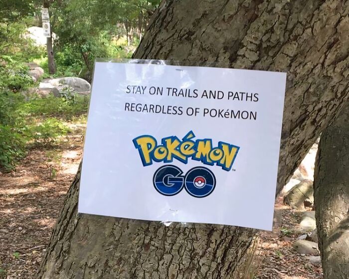 A funny sign in the wild attached to a tree, reading, Stay on trails and paths regardless of Pokémon.