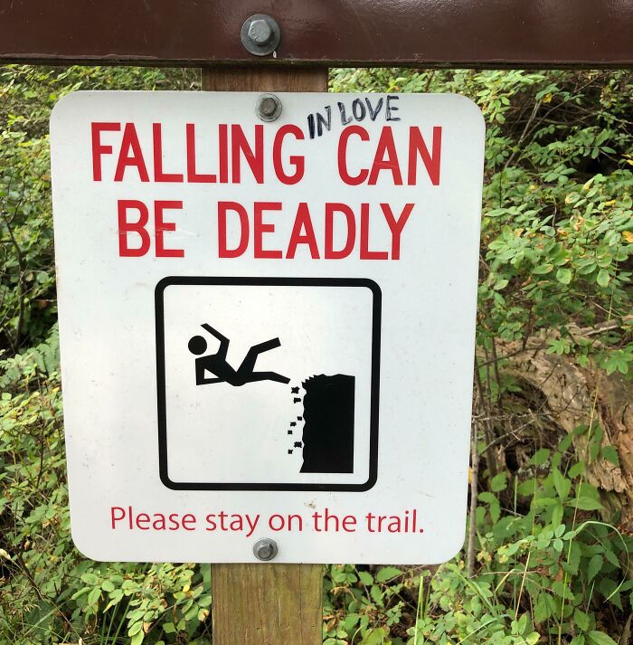 A funny sign on a trail warning that falling in love can be deadly, with a graphic of a person falling.