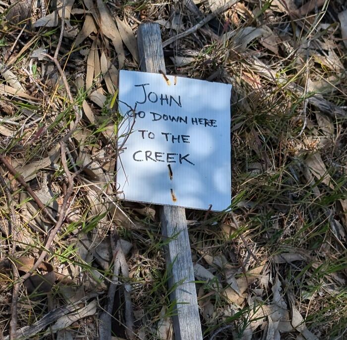 A funny handwritten sign on a stick in the wilderness that says John go down here to the creek, a unique find in the wild.