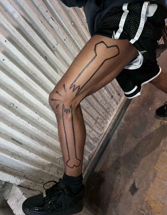 Leg tattoo fail showing cartoonish broken bones outlined in black
