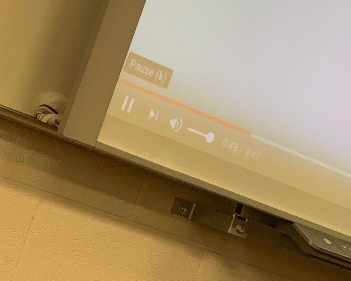 A projector screen displaying a video player with the pause button highlighted, used by annoying teachers.
