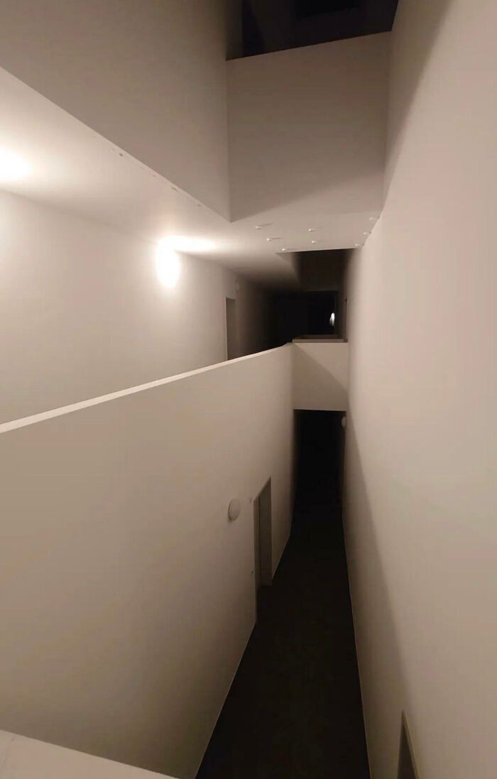 A narrow, stark white hallway with a dark, descending path, embodying a deeply unsettling liminal space.