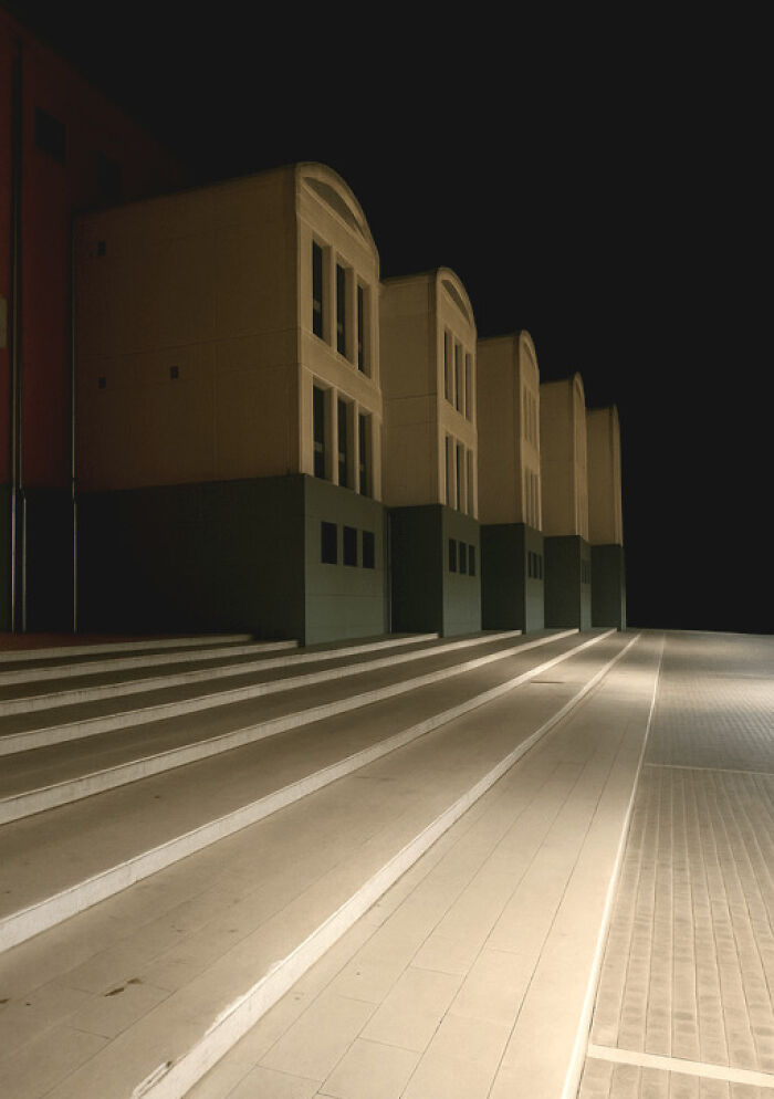 Long row of four pale, unsettling liminal spaces with arched windows at night, dark sky.
