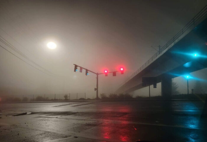 A deeply unsettling liminal space with a hazy, fog-filled road and a traffic light showing red, creating an eerie abyss.