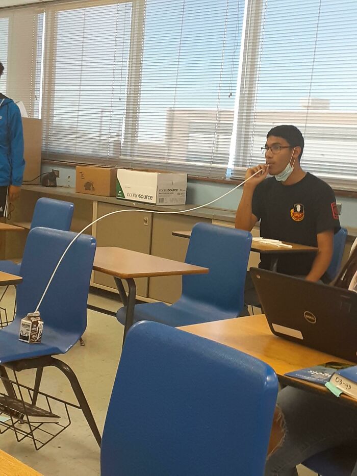 A Mad Lad student sips chocolate milk through a very long straw in a classroom.