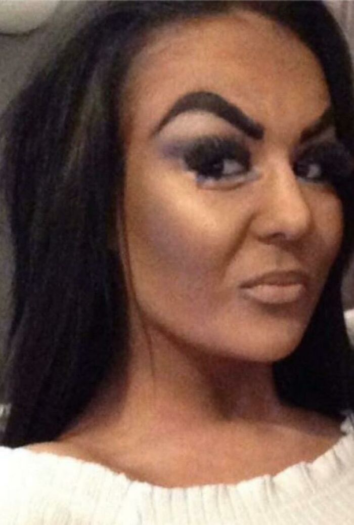 A woman with over-applied makeup, including poorly shaped eyebrows and heavy eye shadow, after a beauty salon visit.
