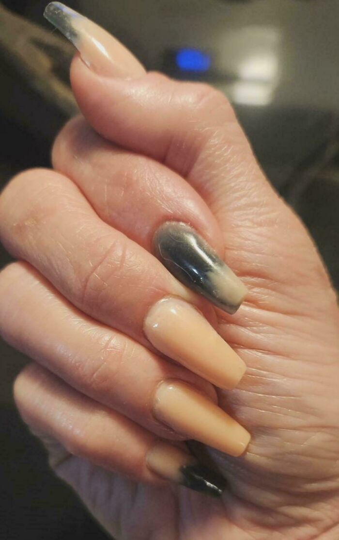 A hand with poorly done ombre acrylic nails, showing discolored and uneven tips from a beauty salon visit.