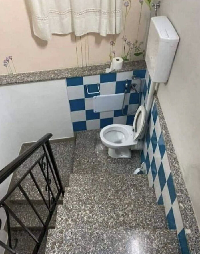 An unhinged real estate listing shows a toilet awkwardly placed on a stairway landing with blue and white tiled walls.