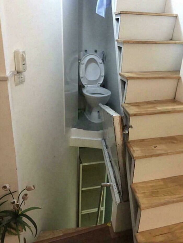 An unhinged real estate listing showing a toilet oddly placed under a staircase, revealing a small, cramped space.