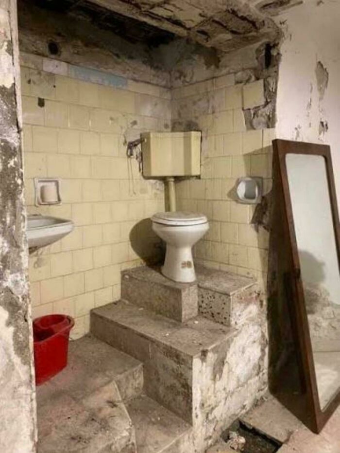 A toilet placed on top of concrete steps in a decrepit bathroom, featured in unhinged real estate listings.