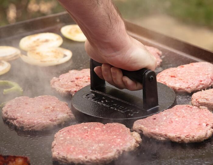 A hand pressing down on raw burger patties with a griddle press, highlighting Prime Day Deals for kitchen gadgets.