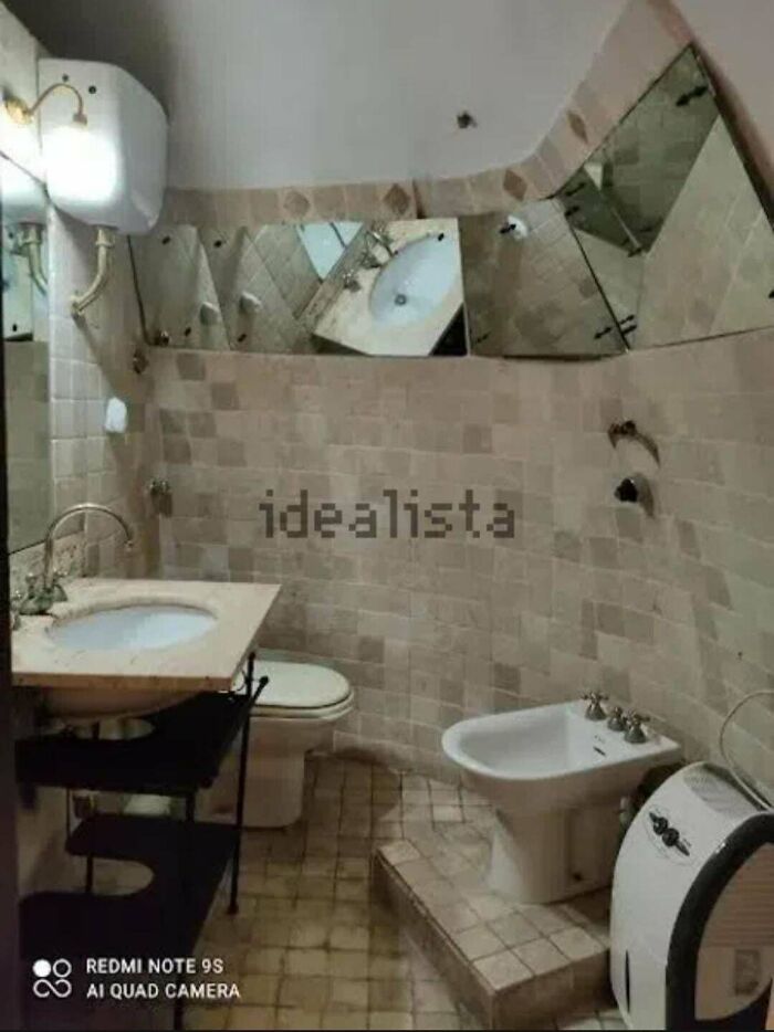A peculiar real estate listing showing a bathroom with irregularly shaped, mismatched mirrors and beige tiles.