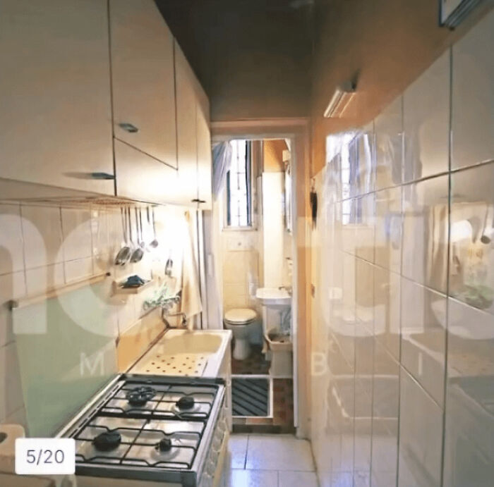 A narrow, unhinged real estate listing kitchen with a stove and sink, leading to a small bathroom.