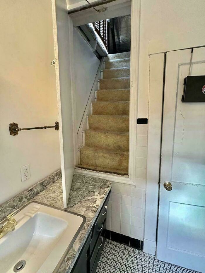 An unhinged real estate listing displaying a strange bathroom layout with a sink and vanity next to an open stairwell.
