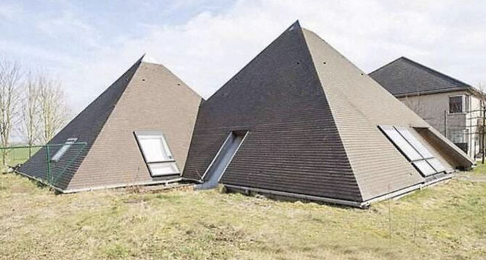 An unhinged real estate listing of two pyramid-shaped houses, appearing unusual and out of place in a grassy field.