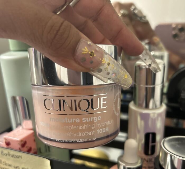 A hand with long decorated nails holds a Clinique Moisture Surge cream, a popular Prime Day deal in beauty.