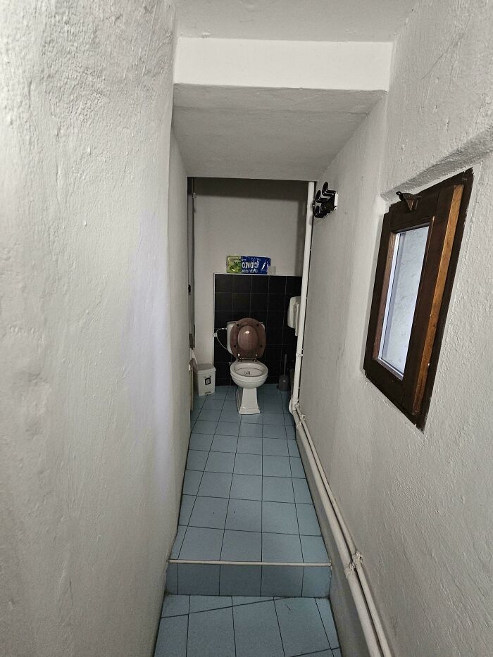 A narrow, unappealing hallway leading to a small, isolated toilet, representing unhinged real estate listings.