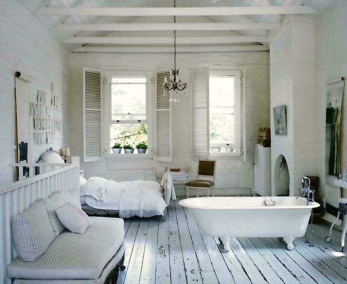 A rustic white bedroom with a claw-foot bathtub at the foot of the bed, a peculiar real estate listing.