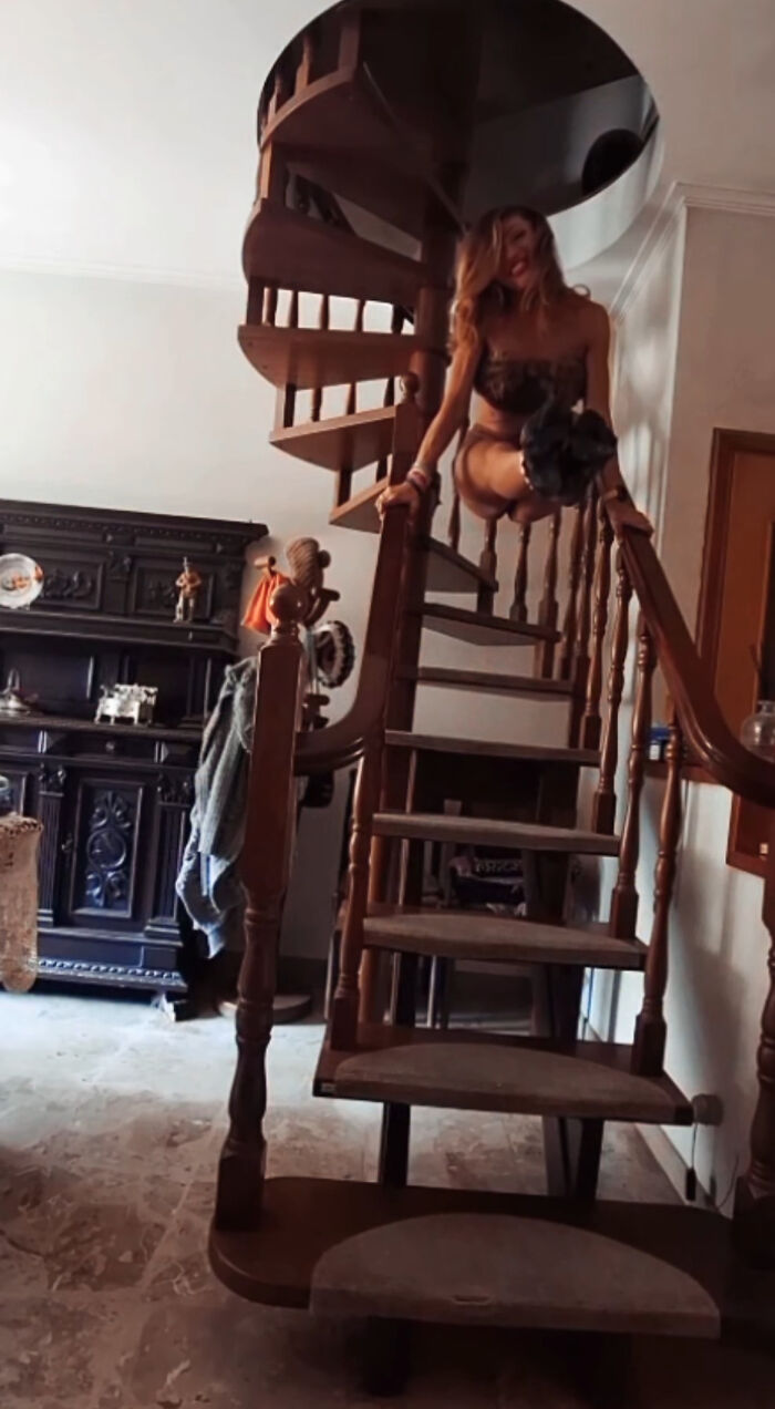 A woman perches precariously on a spiral staircase, an unhinged real estate listing.