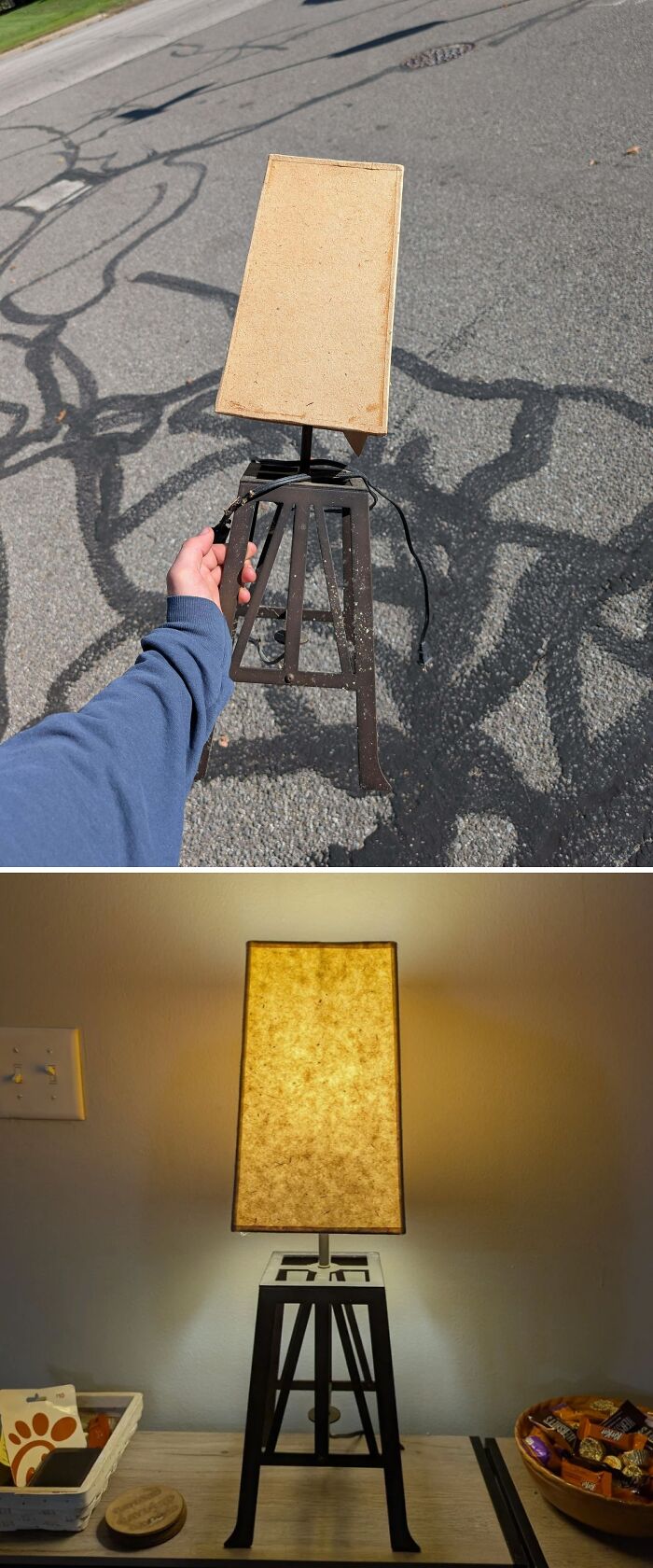 A person holding a lamp base found while dumpster diving, and the lamp lit up on a desk.