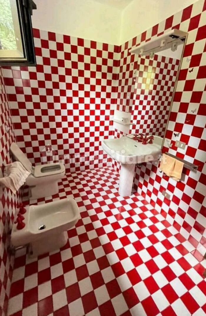 A bathroom with bright red and white checkered tiles covering the walls and floor, a toilet, bidet, and sink, an unhinged real estate listing.