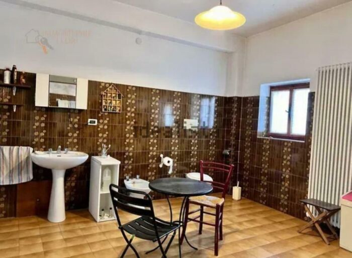An unhinged real estate listing photo of a bathroom with a sink, toilet, bidet, and small table with two chairs.