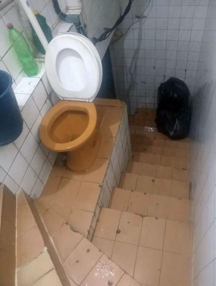 An unhinged real estate listing showing a toilet precariously perched at the top of a short, tiled staircase.