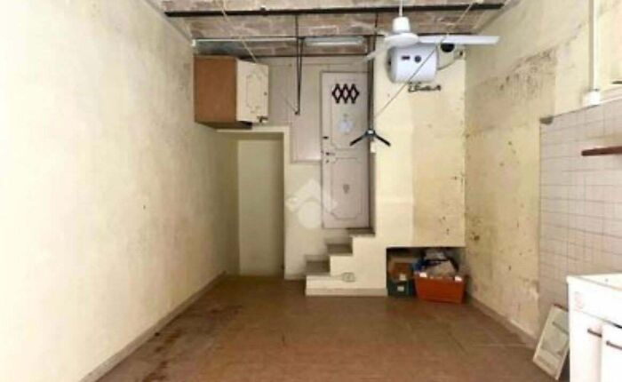 An unhinged real estate listing image of a dirty room with a staircase leading to a small door, and a ceiling fan.