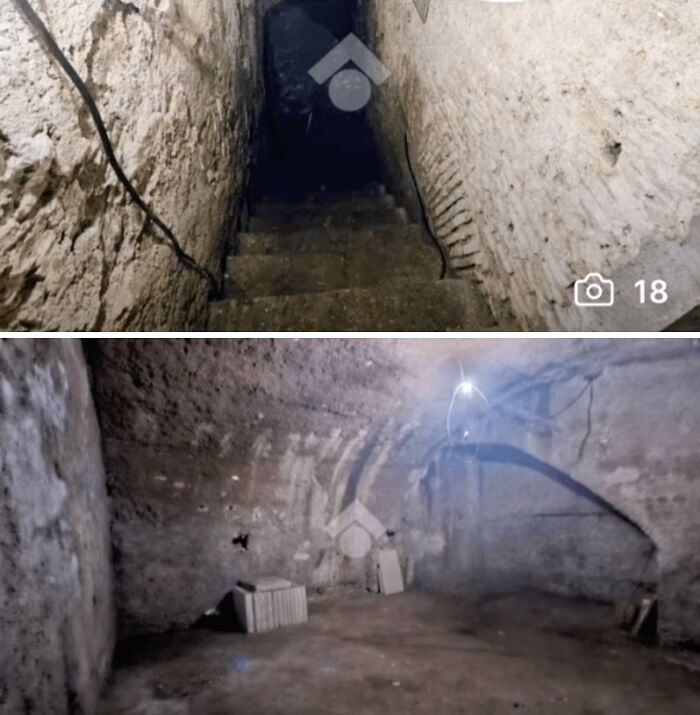 A dark, narrow stairway descends into an unhinged real estate listing's basement with rough stone walls and dim lighting.
