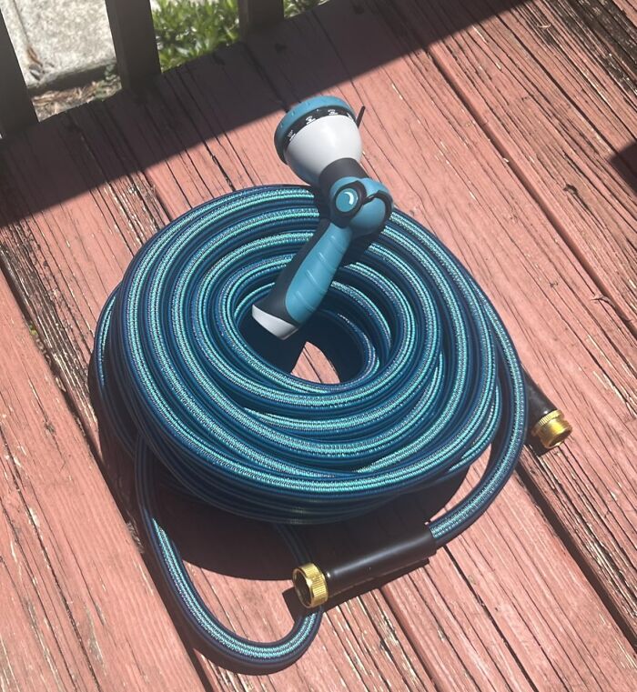 Prime Day outdoor and backyard essentials for summer, a coiled blue garden hose with a spray nozzle on a wooden deck.