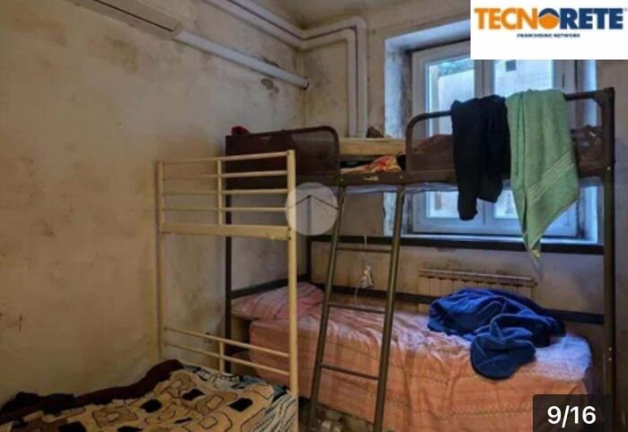 An unhinged real estate listing showing a messy bunk bed in a small, damp room with dirty walls and a window.