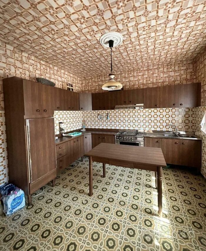 A kitchen with outdated brown patterned wallpaper and floor tiles, an unhinged real estate listing.