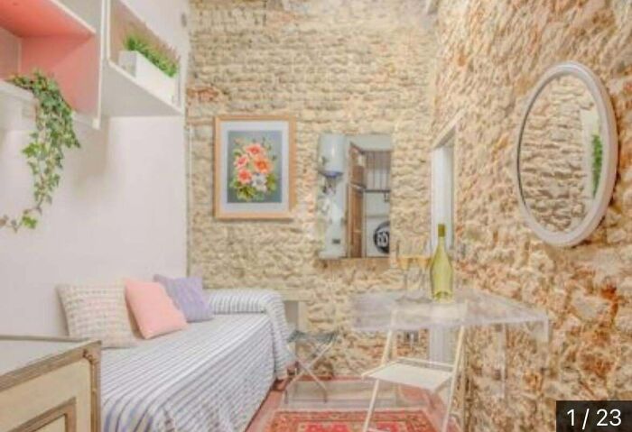 An unhinged real estate listing displays a room with exposed stone walls, a narrow daybed, and a small table.
