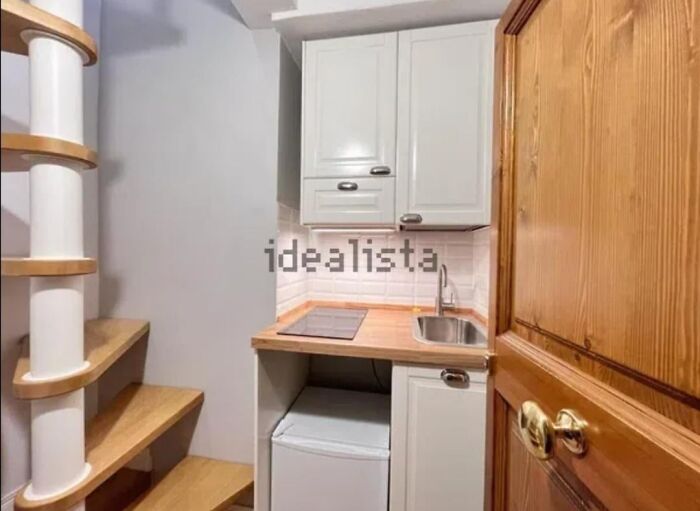 An unhinged real estate listing features a cramped kitchen with a spiral staircase, undersized appliances, and wooden door.