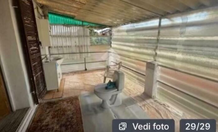 An unhinged real estate listing with a toilet and sink in an outdoor, semi-enclosed patio area.