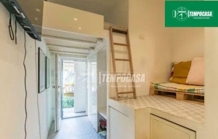 A compact real estate listing with a small living area, a wooden ladder to a loft, and a sofa made of pallets.